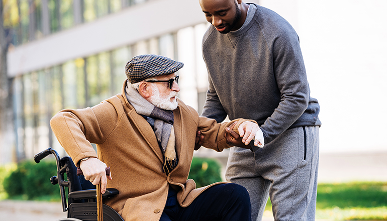 A man helping an older gentleman walk with his cane.