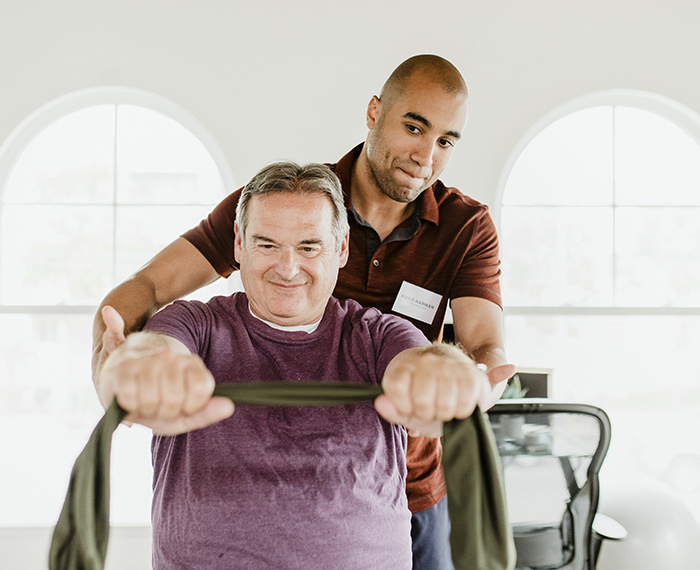 A man helping another man exercise on a machine.